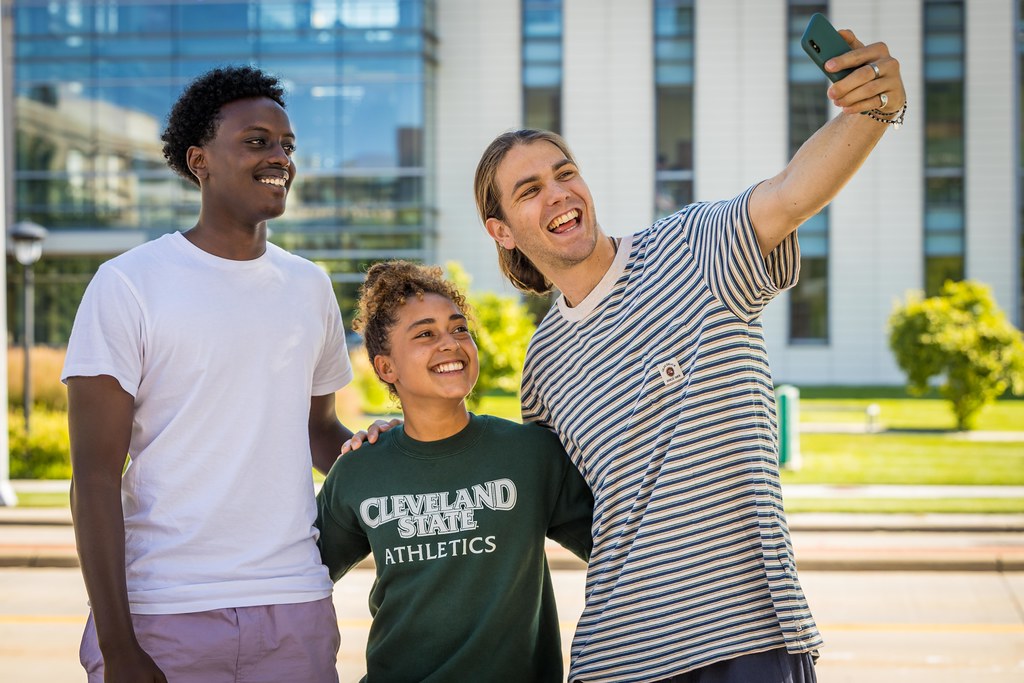 Three students standing together taking a picture on a phone.