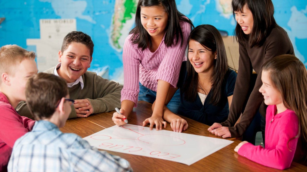 Middle-school-aged students gathered around a table working on an activity together