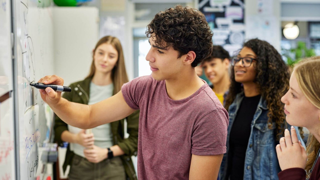 High school-aged students writing on a whiteboard in a class