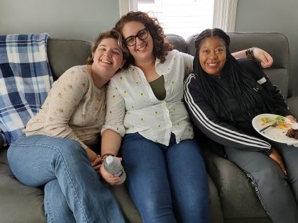Three staff members sitting on a couch together with a plate of food