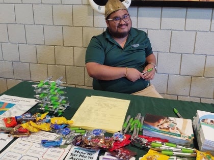 Intern in green shirt with viking hat in front of table of mental health brochures and swag items