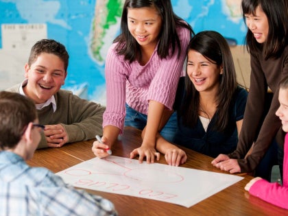 Middle-school-aged students gathered around a table working on an activity together