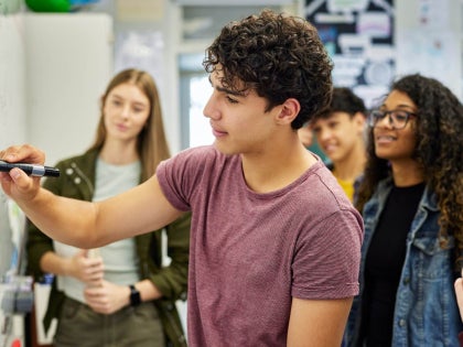 High school-aged students writing on a whiteboard in a class